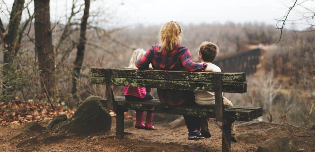 Mom and two kids sitting on bench in forest