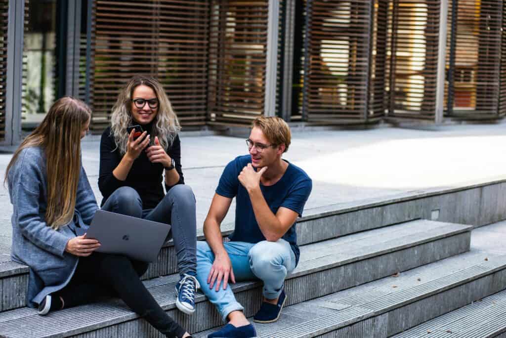 young adult guy and two girls sitting on steps outdoors