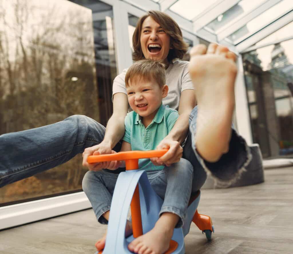 child driving toy and mom riding behind