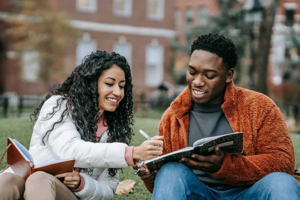 couple students working on homework on lawn smiling