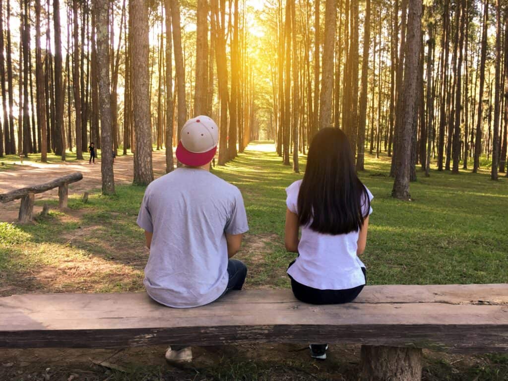 Young couple backs looking through trees at sun path