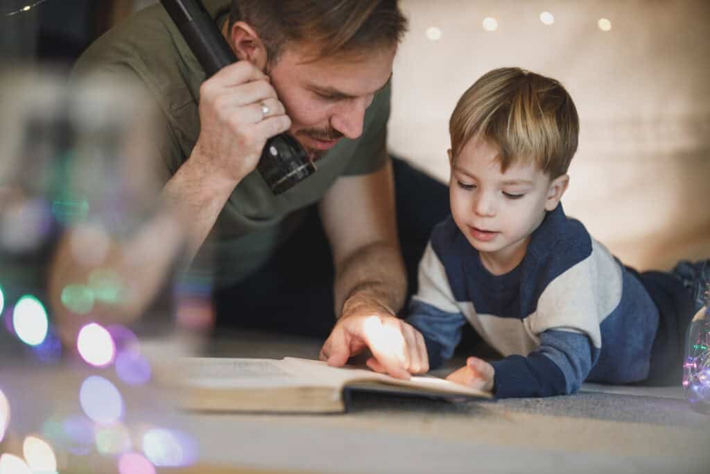 Dad and young son reading by flashlight